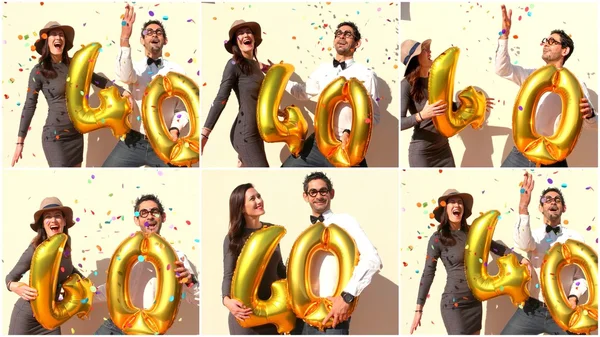 Alegre pareja celebra un cumpleaños de cuarenta años con grandes globos dorados y pequeños trozos de papel coloridos en el aire . —  Fotos de Stock