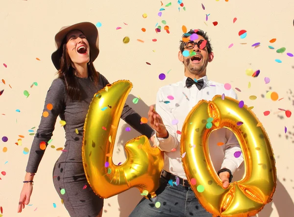 Alegre pareja celebra un cumpleaños de cuarenta años con grandes globos dorados y pequeños trozos de papel coloridos en el aire . — Foto de Stock