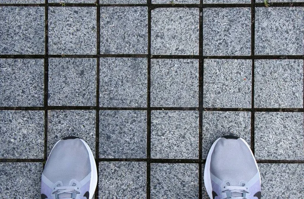 Gri fayansların üzerindeki spor ayakkabıların üzerinde ayaklar 