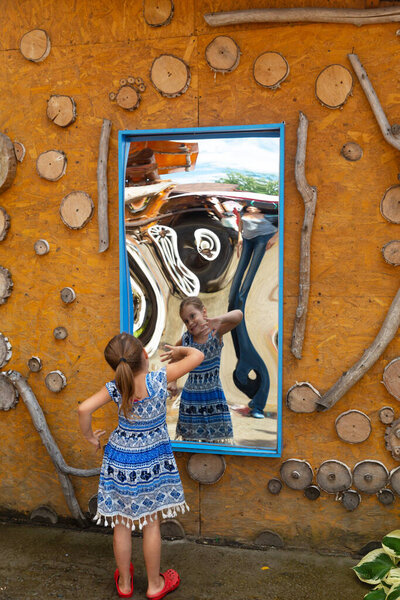 Little sweetheart makes a face in front of a crooked mirror in the park