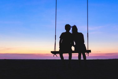 Genç çift salıncakta oturuyor Romantik bir siluet tarzıyla