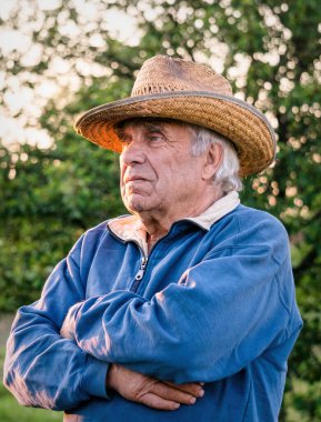 Akşam bahçesinin arka planında hasır şapkalı yaşlı bir adam.