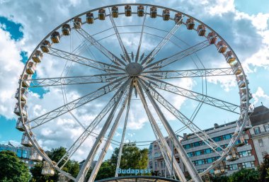Budapeşte / Macaristan - 14 Temmuz 2019: Modern güzel dönme dolap, yaz fırtınalı bir gökyüzü ve yeşil bir parkın arka planında. Macaristan, Budapeşte 'nin ünlü turistik merkezi
