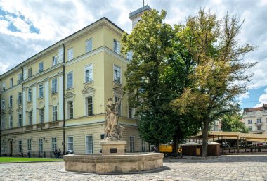 Lviv şehri, Ukrayna - 01 Mayıs 2019: Adonis 'in antik heykeli ve arka planda Lviv Belediye Binası ve eski tarihi Pazar Meydanı binasının ön cephesine karşı bir taş çeşme