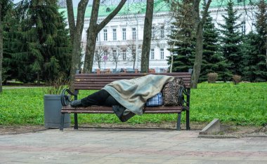 Poltava, Ukrayna - 14 Nisan 2021: Ukrayna 'nın Poltava kentinde bir bahar sabahı parktaki bankta uyuyan evsiz yaşlı kadın. Avrupa 'da sosyal sorunlar, evsizlik ve işsizlik. Durgunluk ve koronavirüs salgınının sonuçları.