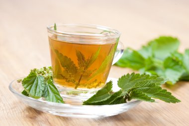 Hot nettle tea with stinging nettle inside teacup on a wooden floor clipart