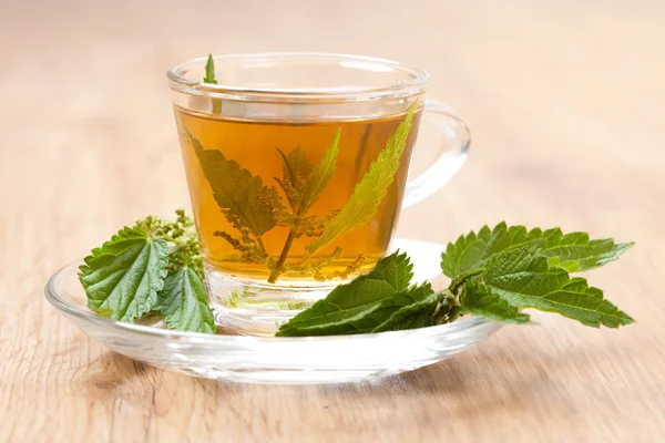 Té de ortiga fresco y saludable en el suelo de madera, florecer dentro de la taza de té —  Fotos de Stock