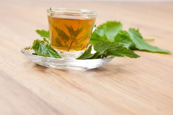 Té hecho de ortiga en el suelo de madera, con algunos racimos de ortiga fresca en el fondo una flor de ortiga dentro de la taza de té —  Fotos de Stock