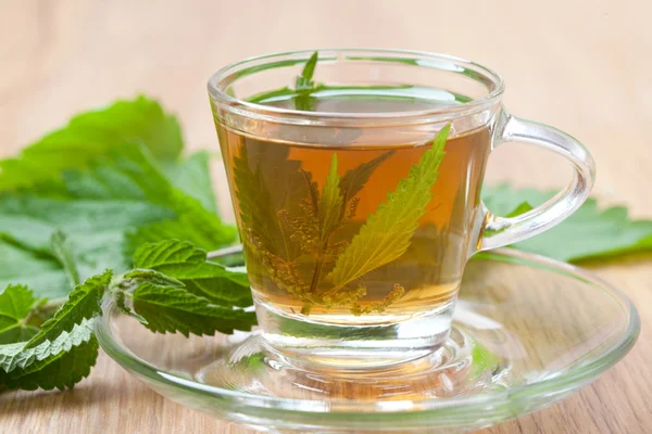 Té de ortiga saludable con hoja de ortiga fresca en vidrio, en suelo de madera —  Fotos de Stock