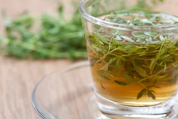 Té de tomillo medicinal con hojas frescas dentro de la taza de té y un montón de tomillo en el fondo, suelos de madera — Foto de Stock