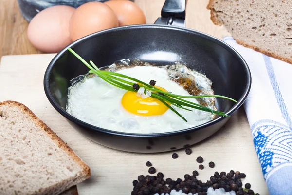 Breakfast with fried egg in frying pan with spice, bread, on wooden plate — Stock Photo, Image