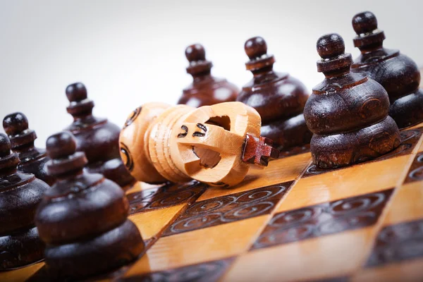 Checkmated chess king on wooden chessboard surrounded by enemies — Stock Photo, Image