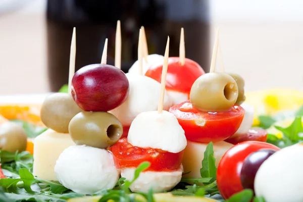 Comida mediterrânica com palitos de queijo, uvas, tomate cereja, mussarela e garrafa de videira vermelha , — Fotografia de Stock