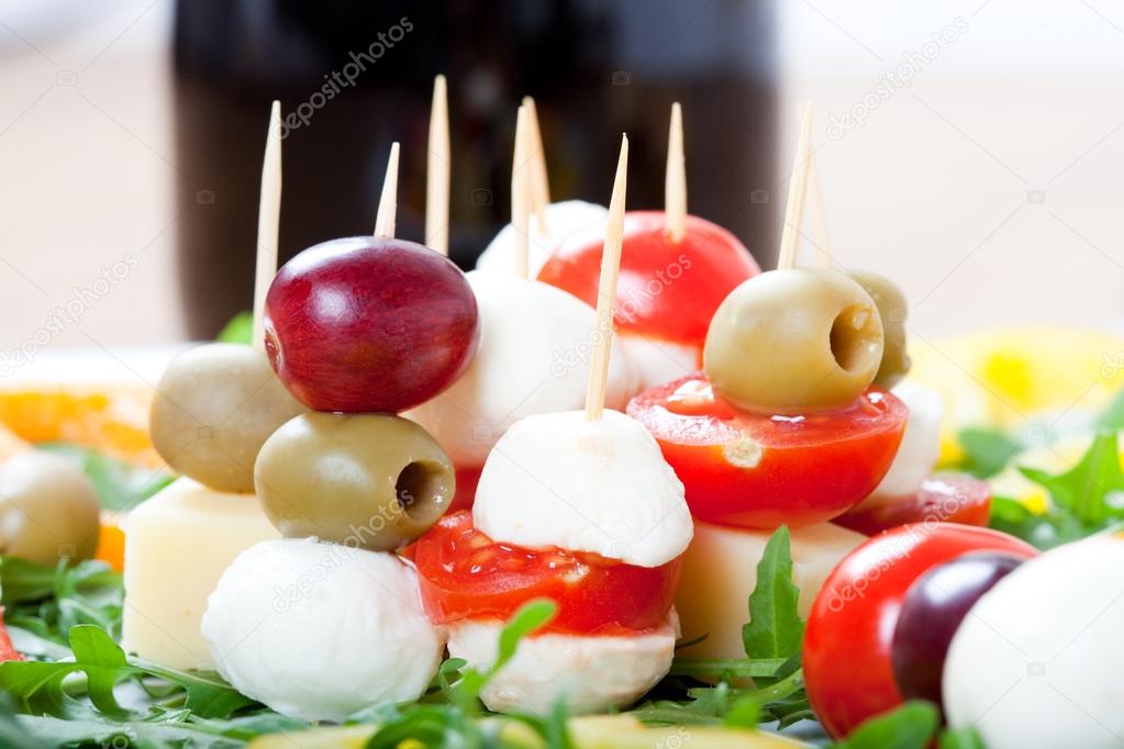 Mediterranean finger food with cheese sticks, with grapes, cherry tomatoes, mozzarella and bottle of red vine,
