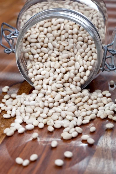 Heap of white beans falling out of glass bowl on a old wooden table — Stock Photo, Image