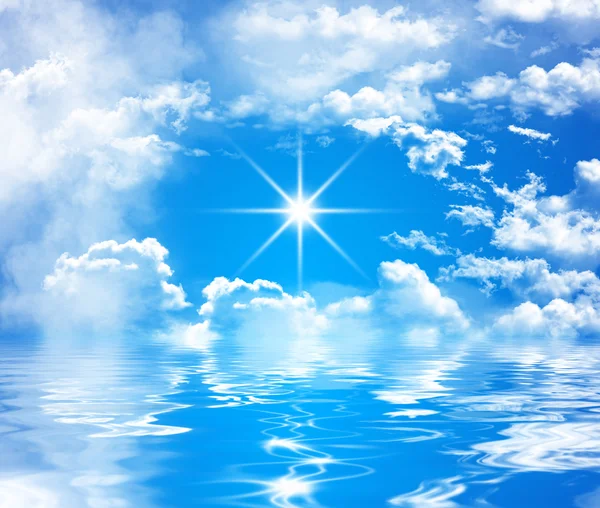 Blue sky with big clouds and shiny sun over water with waves and reflection