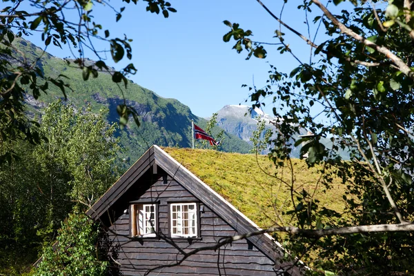 Holzhaus mit Gras auf dem Dach und norwegischer Flagge inmitten von Bergen mit Gletschern — Stockfoto