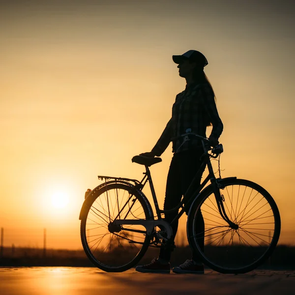 Bella ragazza hipster con una bicicletta sulla strada durante il tramonto — Foto Stock