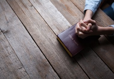Elleri, tahtadan bir masanın üzerinde, bir İncil 'le dua ediyor.