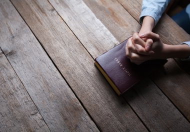 hands praying with a bible in a dark over wooden table clipart