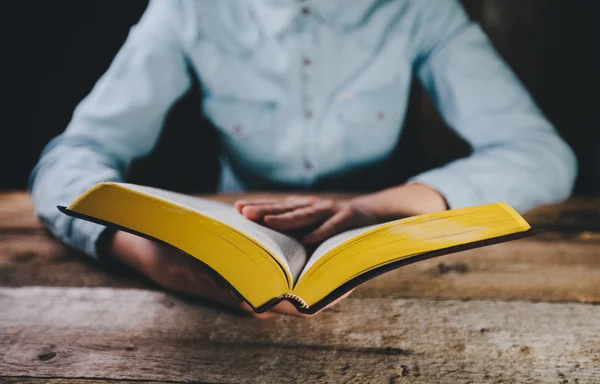 Mains de femme priant avec une bible dans l'obscurité sur une table en bois — Photo