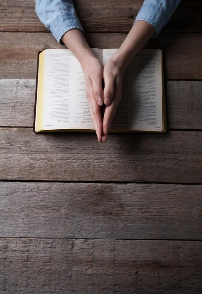 Mani di donna che pregano con una bibbia in un tavolo di legno scuro — Foto Stock