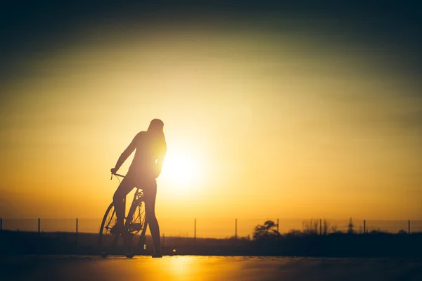 Linda garota hipster com uma bicicleta na estrada durante o pôr do sol — Fotografia de Stock