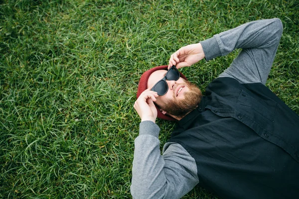 Ragazzo hipster che indossa occhiali da sole e sdraiato sull'erba — Foto Stock