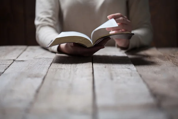 Frauenhände beten mit einer Bibel auf einem dunklen Holztisch — Stockfoto