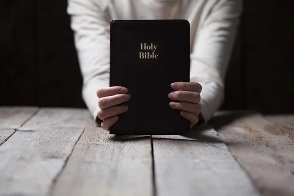 Kobieta ręce modląc się z Biblii w ciemno na drewnianym stole — Zdjęcie stockowe