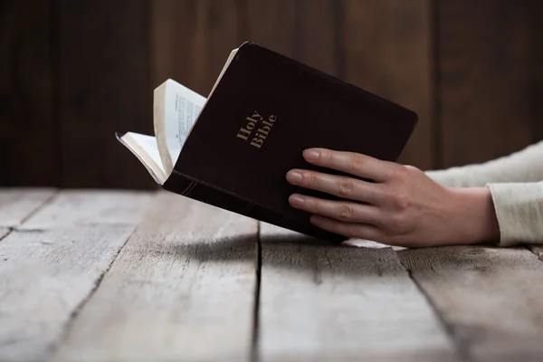 Manos de mujer rezando con una Biblia en una mesa oscura sobre madera —  Fotos de Stock