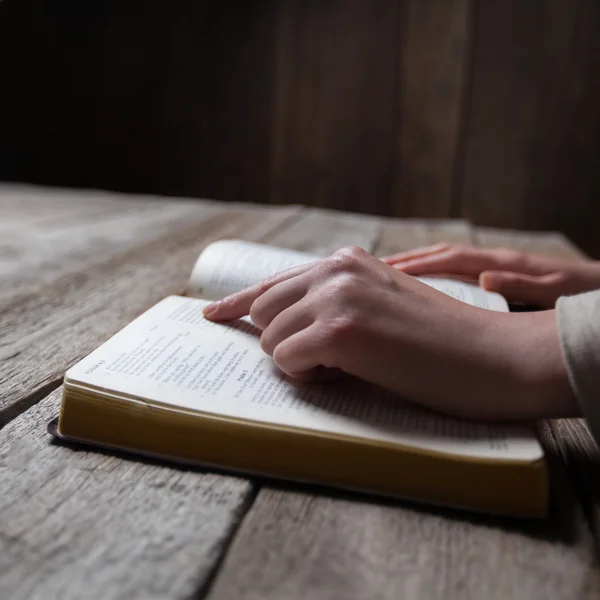 Kobieta ręce modląc się z Biblii w ciemno na drewnianym stole — Zdjęcie stockowe