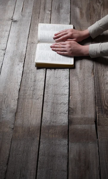 Manos de mujer rezando con una Biblia en una mesa oscura sobre madera — Foto de Stock