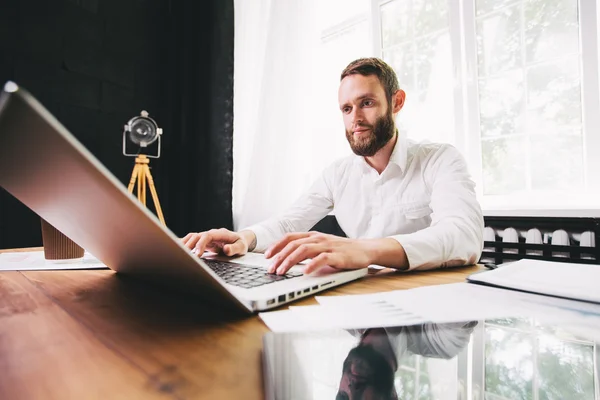 Mann arbeitet im Büro neben einem Fenster mit einem Laptop — Stockfoto