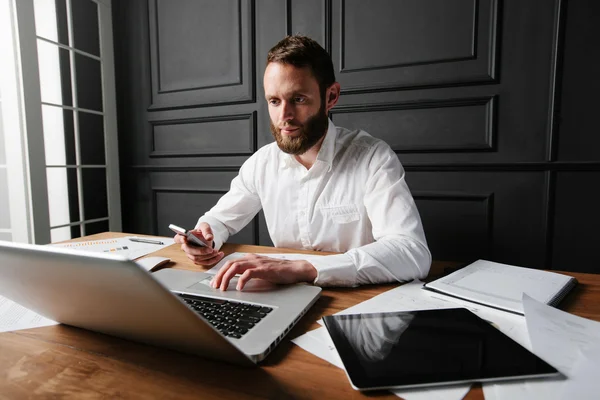 Homem trabalhando no escritório ao lado de uma janela usando um laptop — Fotografia de Stock