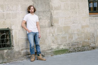 Hipster yakışıklı erkek manken beyaz boş tişört giyiyor. Logonuz için yeri var. Ya da Avrupa sokaklarında gelişigüzel tasarlanmış.