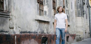 Hipster yakışıklı erkek manken beyaz boş tişört giyiyor. Logonuz için yeri var. Ya da Avrupa sokaklarında gelişigüzel tasarlanmış.