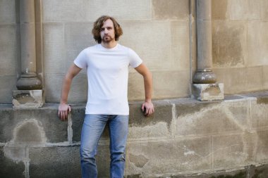 Hipster yakışıklı erkek manken beyaz boş tişört giyiyor. Logonuz için yeri var. Ya da Avrupa sokaklarında gelişigüzel tasarlanmış.