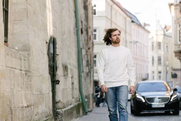 Man wearing white sweatshirt or hoodie for mock up, logo designs or design prints with with free space among europe city streets.