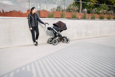 Modern şehir sokaklarında bir bebek arabasıyla gezen ve sonbaharda dinlenen bir anne.