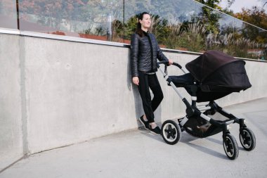 Modern şehir sokaklarında bir bebek arabasıyla gezen ve sonbaharda dinlenen bir anne.