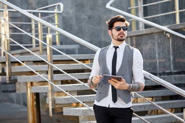 Şehir caddesinde üzerinde şık kıyafetler olan bir tablet kullanan bir iş adamı.