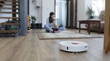Anne ve çocuk evde oynarken robot elektrikli süpürge oturma odasını temizliyor. Otomatik elektrik süpürgesi