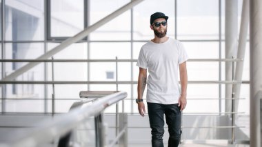 Hippi, gözlüklü, beyaz, boş tişörtlü ve logonuz için geniş siyah kotlu yakışıklı bir erkek model.