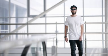 Hippi, gözlüklü, beyaz, boş tişörtlü ve logonuz için geniş siyah kotlu yakışıklı bir erkek model.