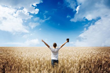 Man holding up Bible in a wheat field clipart