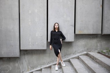 Fashion portrait of a sexy brunette woman with a make up wearing black clothes. She is wearing black modern dress, white sneakers and glasses