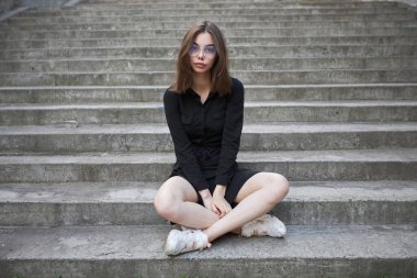 Woman in black dress sitting on cement stairs in summer in urban city area. She is happy and relaxed
