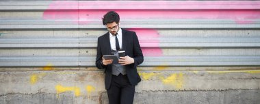 Şehir caddesinde üzerinde şık kıyafetler olan bir tablet kullanan bir iş adamı.