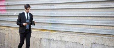 Şehir caddesinde üzerinde şık kıyafetler olan bir tablet kullanan bir iş adamı.